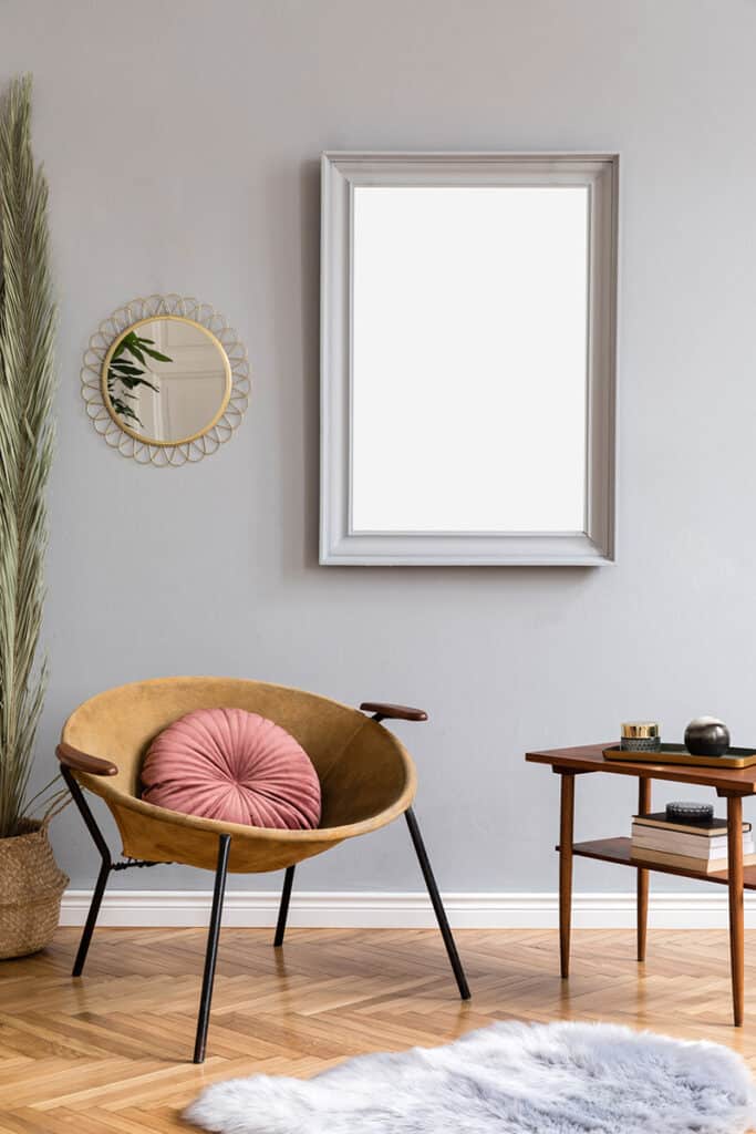 Coin détente de style rétro avec un miroir rectangulaire accroché un mur. Il a un cadre blanc. Un autre petit miroir rond est accroché à côté et ressemble à un soleil. Une chaise jaune avec des pieds noirs est posée sur le parquet près d'une petite table en bois.